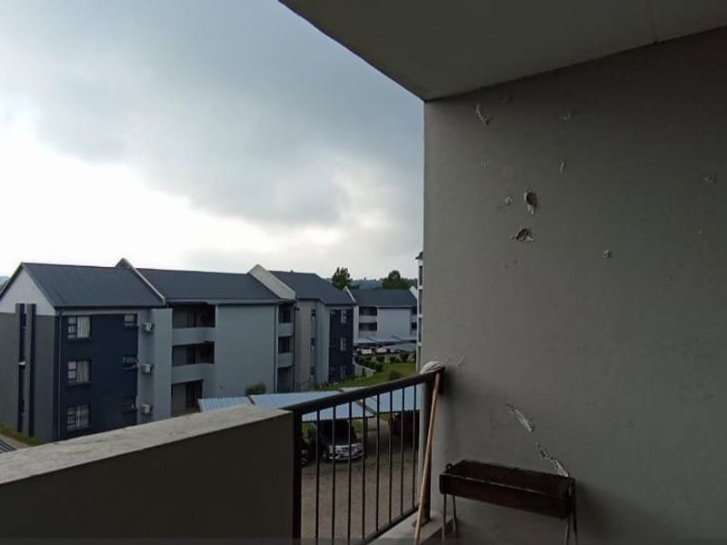 A balcony area with a metal balustrade and views over the apartment complex, showing signs of wear on the exterior wall finish.