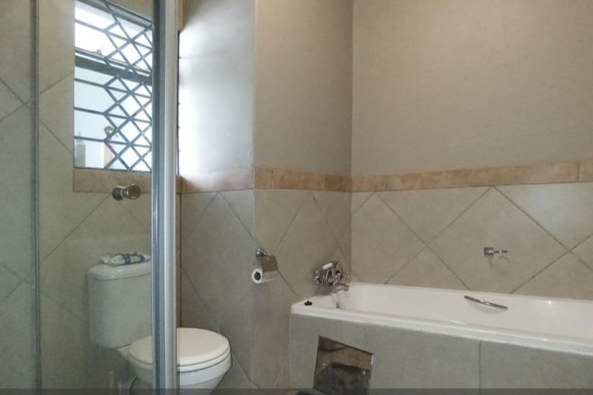 A functional bathroom featuring a bathtub, separate shower enclosure, and toilet, finished with neutral wall tiling and a window with security bars.