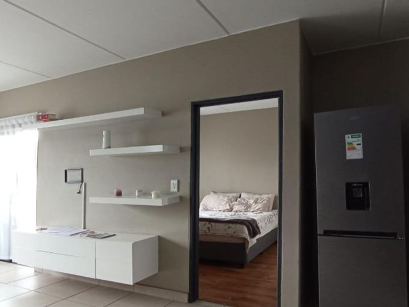 Open plan living area featuring neutral wall tones, tiled flooring, and built-in shelving, with a direct view into the adjacent bedroom.