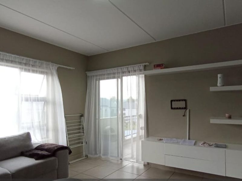 A bright living room featuring tiled floors, built-in floating shelves, a media console, and sliding glass doors leading to an outdoor balcony.