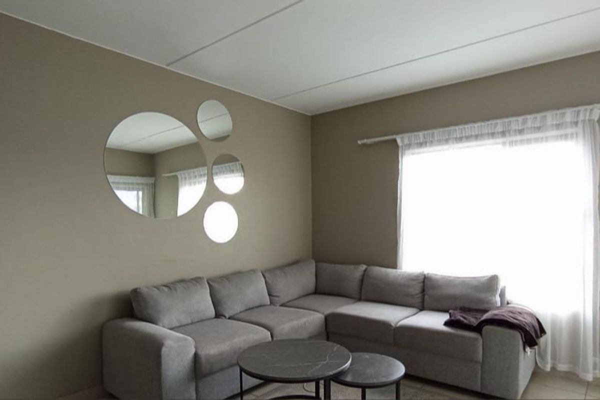 A living room featuring neutral-toned walls, tiled flooring, and a large window with a curtain rod.