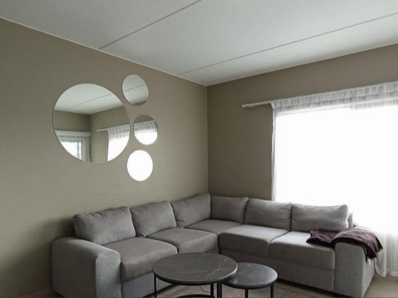 A living room featuring neutral-toned walls, tiled flooring, and a large window with a curtain rod.