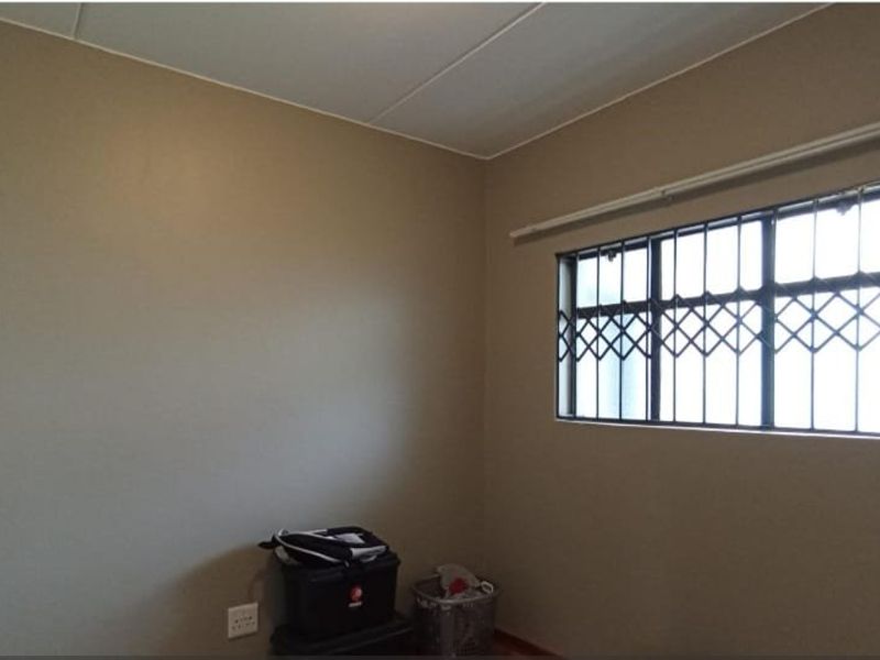 A simple, empty bedroom featuring neutral wall paint and a window fitted with a security gate.