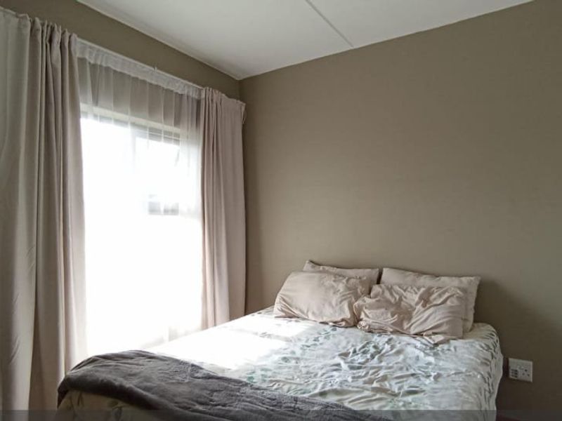 A bedroom featuring neutral wall tones, a sliding window with curtains, and a built-in cupboard with an arched frame.
