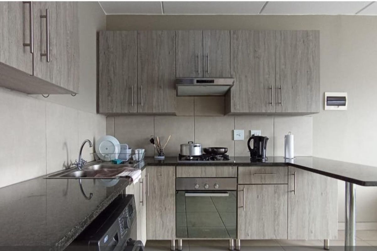 Modern kitchen featuring wood-grain cabinetry, granite countertops, a breakfast bar, and integrated stainless steel appliances including a gas hob and oven.
