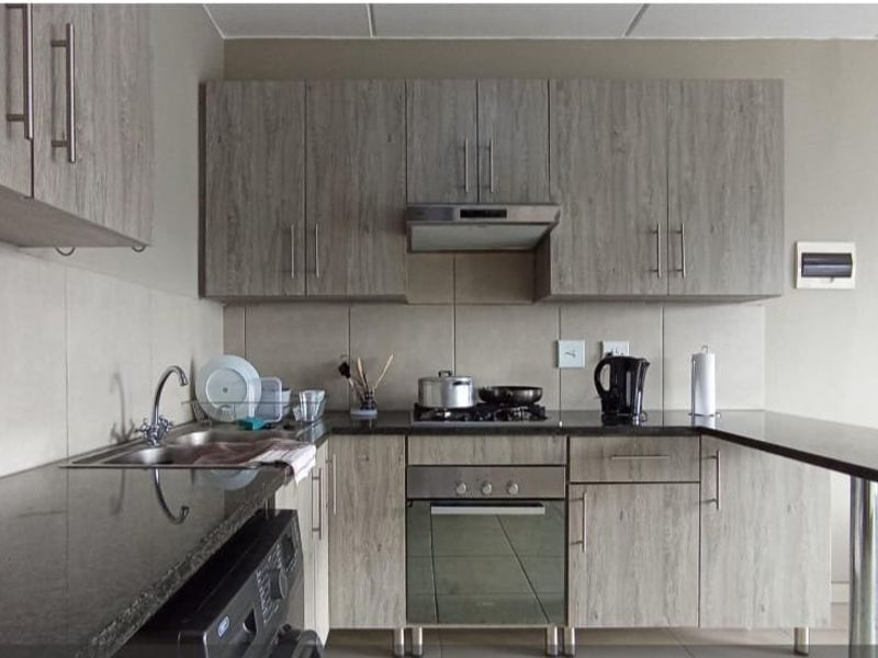 Modern kitchen featuring wood-grain cabinetry, granite countertops, a breakfast bar, and integrated stainless steel appliances including a gas hob and oven.
