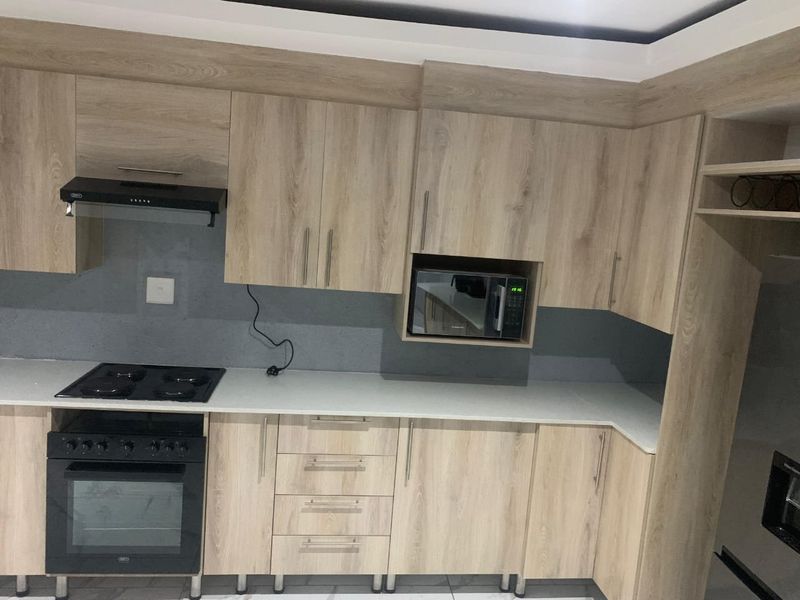 Modern kitchen featuring light wood-grain cabinetry, stone countertops, and integrated appliances including an oven, hob, and microwave.