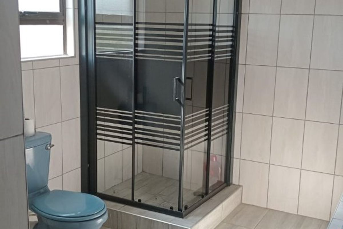 A functional bathroom featuring a corner shower enclosure, tiled flooring and walls, and a standard toilet.
