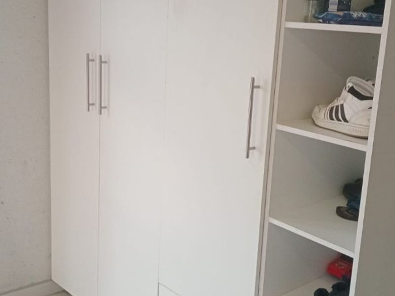 A bedroom featuring a white built-in wardrobe with integrated shelving and drawers, complemented by neutral tiled flooring.