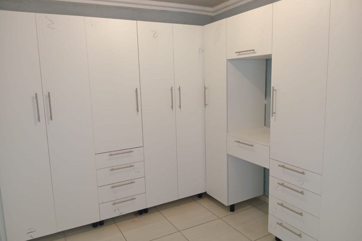 A bedroom featuring extensive white built-in cupboards with an integrated vanity station and tiled flooring.