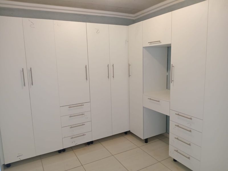 A bedroom featuring extensive white built-in cupboards with an integrated vanity station and tiled flooring.