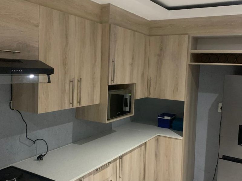 Modern kitchen featuring light wood-grain cabinetry, stone-look countertops, tiled flooring, and integrated appliances including a built-in microwave and extractor fan.