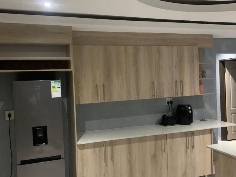 Modern kitchen featuring light wood-grain cabinetry, stone countertops, and contemporary tiled flooring with a decorative recessed ceiling detail.