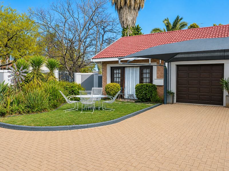 Front view of the property featuring a paved driveway, double garage with shade sail, and a well-maintained garden area.