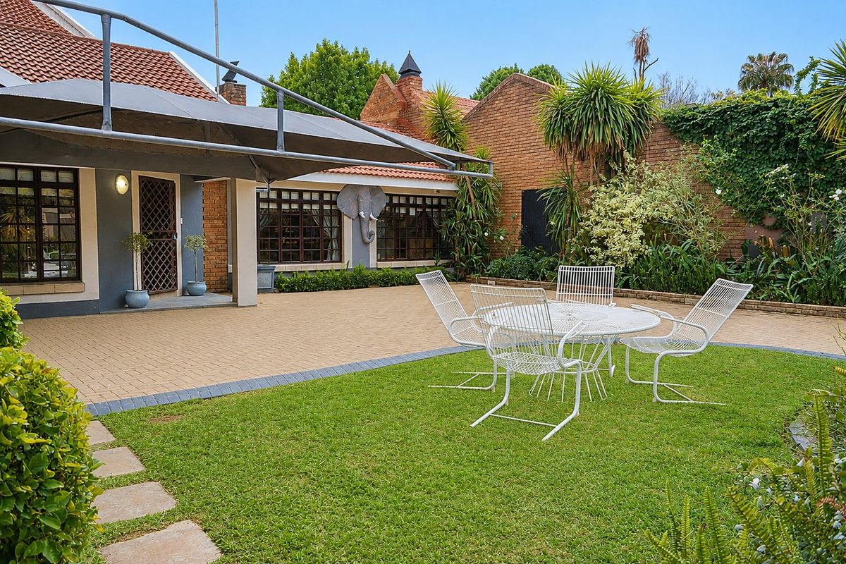 A well-maintained rear garden featuring brick paving, a lawn area, and a shade sail covering the patio space adjacent to the house.