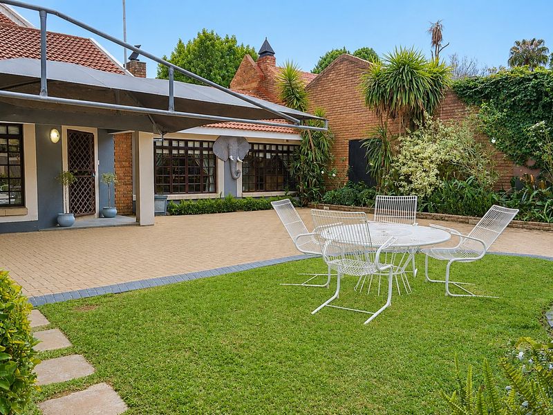 A well-maintained rear garden featuring brick paving, a lawn area, and a shade sail covering the patio space adjacent to the house.