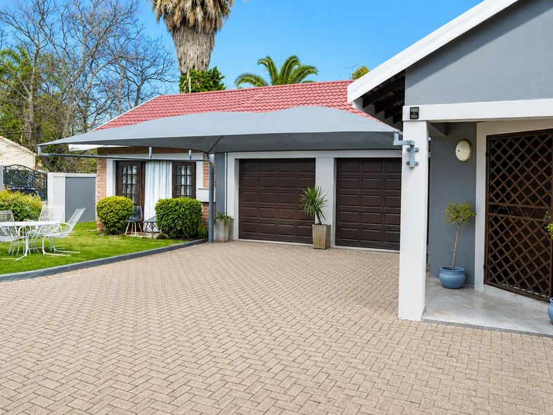 Front exterior view featuring a paved driveway, double garage with shade sail, and a secure entrance with a decorative security gate.