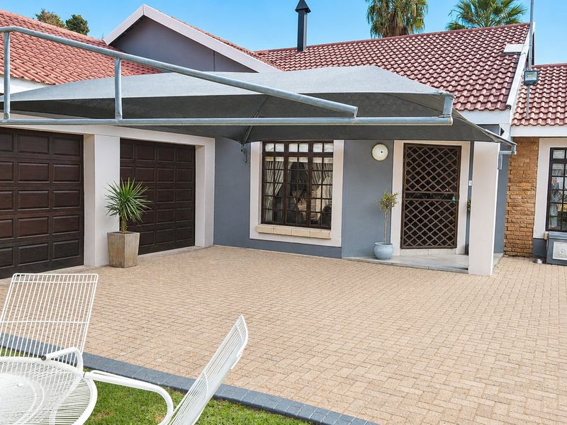 Front exterior view featuring a paved driveway, double garage, and a shade sail covering the entrance area with a tiled roof.