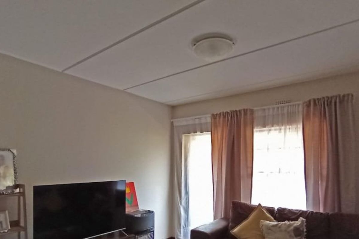 A living room featuring a tiled ceiling, a central light fixture, and a sliding glass door providing natural light.