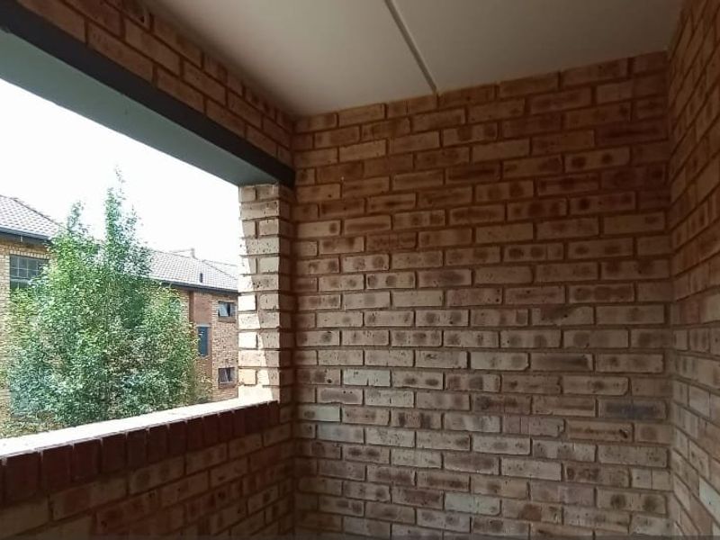 A covered balcony featuring exposed brick walls and a view of the surrounding apartment complex.
