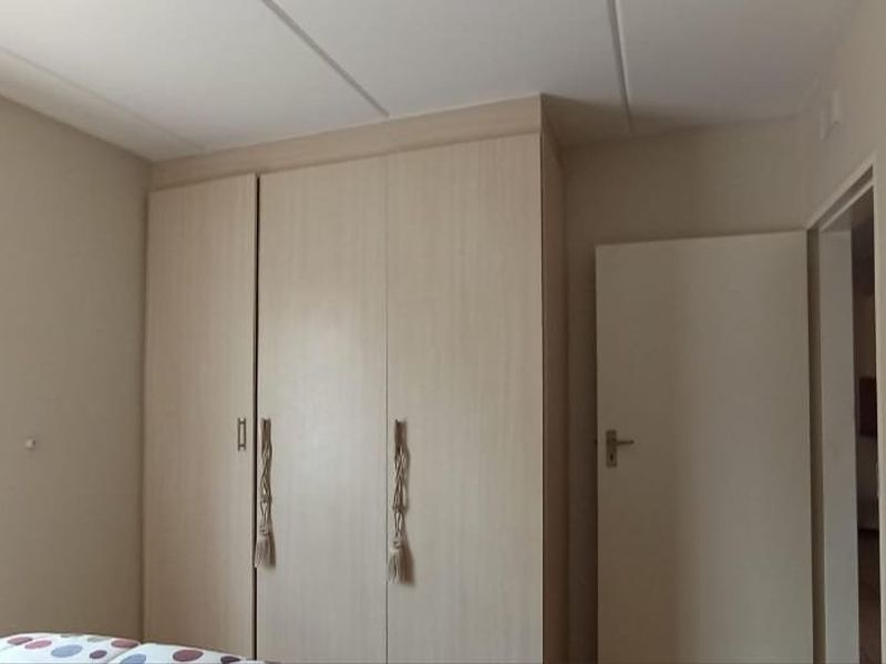 A bedroom featuring neutral walls, a drop ceiling, and light-toned built-in cupboards providing ample storage space.