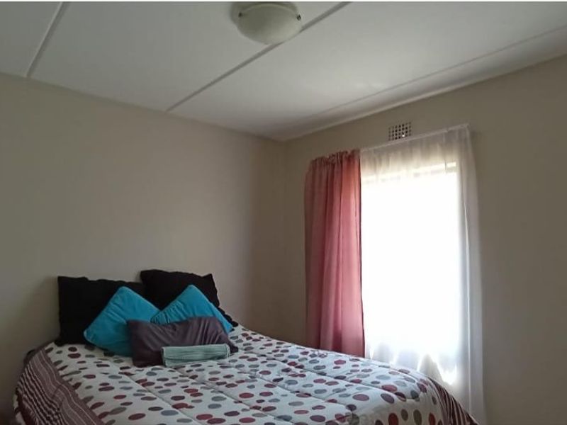 A simple bedroom featuring neutral walls, a ceiling light fixture, and a window with natural light.