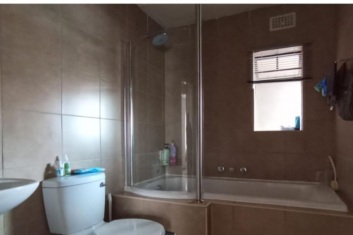 A functional bathroom featuring a pedestal basin, toilet, and a combined bathtub with a glass shower screen and tiled wall finishes.