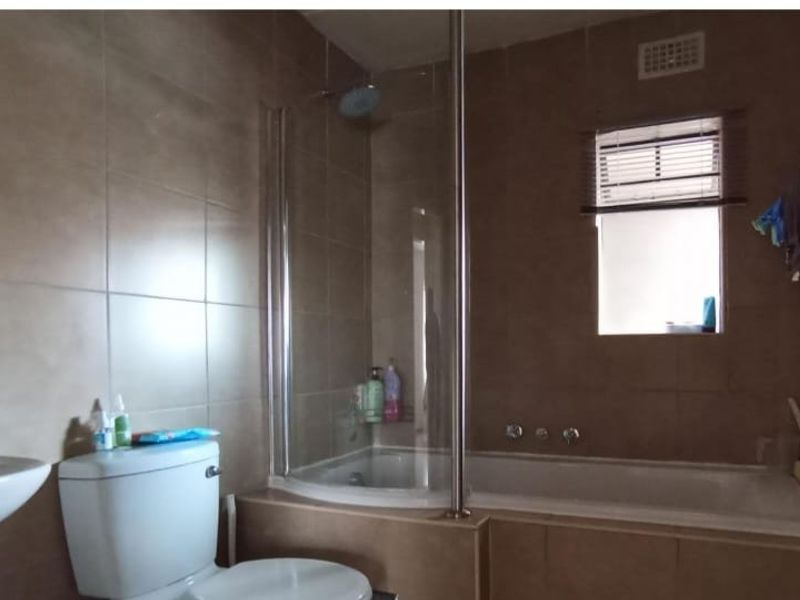 A functional bathroom featuring a pedestal basin, toilet, and a combined bathtub with a glass shower screen and tiled wall finishes.