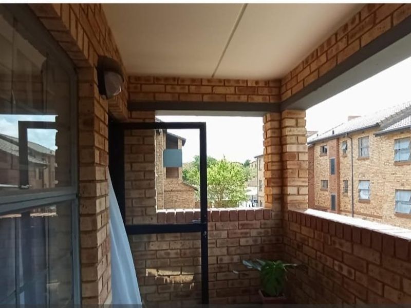A covered balcony featuring exposed face brick walls and steel window frames, offering an open view of the surrounding apartment complex.