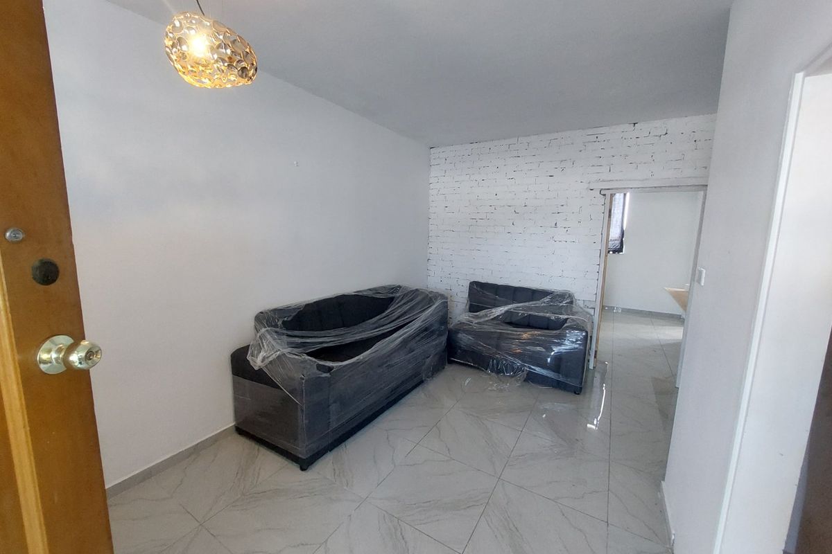 Living area featuring white painted exposed brick wall, modern large-format tile flooring, and a contemporary pendant light fixture.