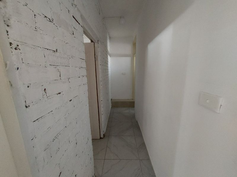 A narrow interior hallway featuring white-painted exposed brickwork, tiled flooring, and simple architectural finishes, providing access to adjacent rooms.