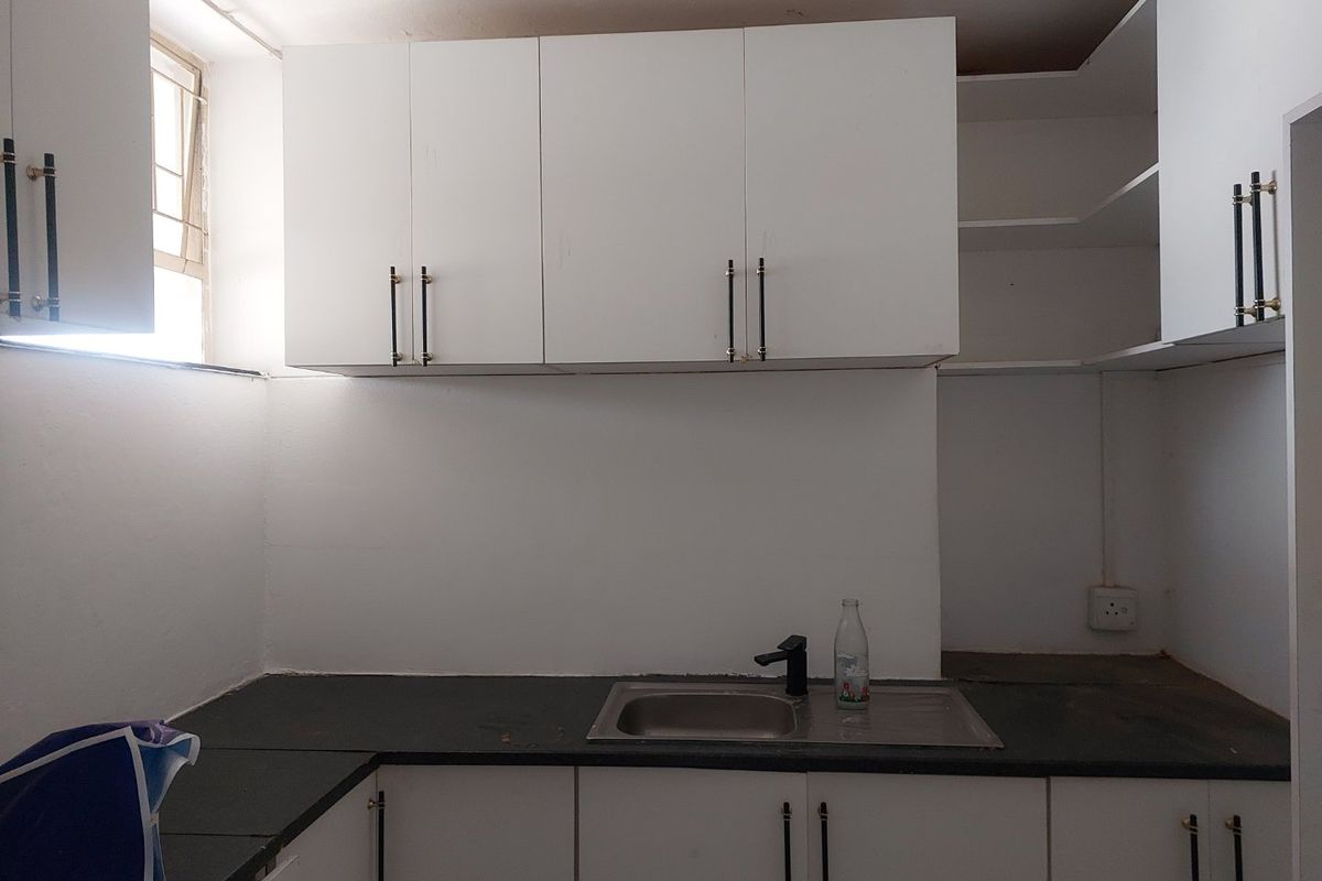 A compact kitchen featuring white cabinetry, dark stone countertops, and a stainless steel sink. The space is currently vacant and requires minor finishing touches.