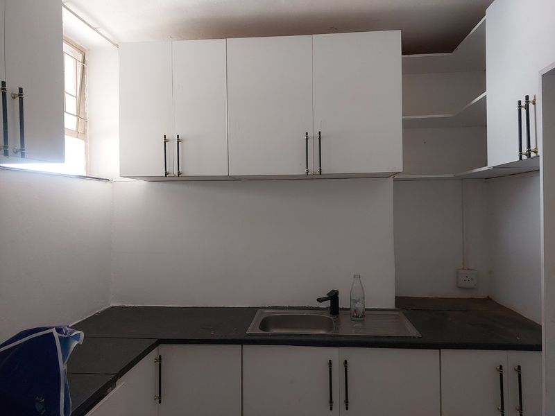 A compact kitchen featuring white cabinetry, dark stone countertops, and a stainless steel sink. The space is currently vacant and requires minor finishing touches.