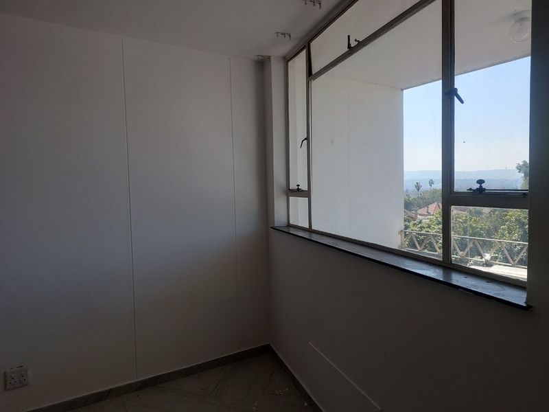An empty bedroom featuring large metal-framed windows that provide natural light and views, finished with tiled flooring.