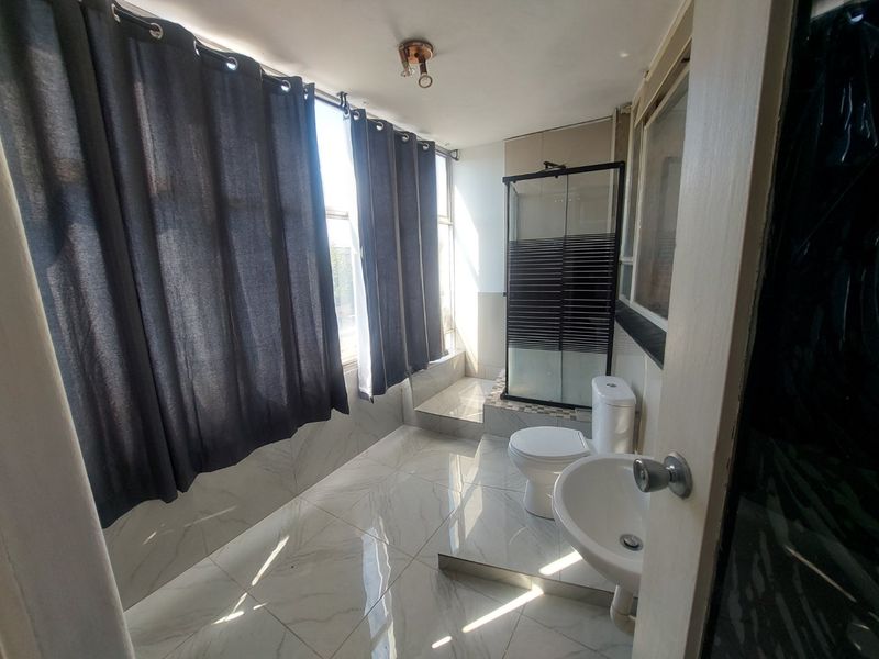 A bright bathroom featuring a shower enclosure, pedestal basin, and toilet, finished with modern marble-look floor and wall tiles.