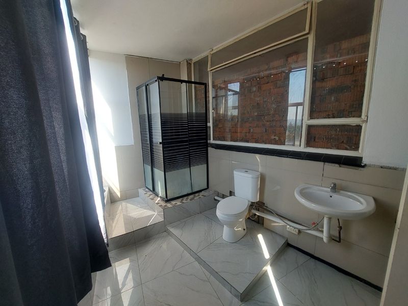 A bathroom featuring a shower enclosure, toilet, and pedestal basin, with unfinished wall sections and exposed brickwork requiring cosmetic attention.