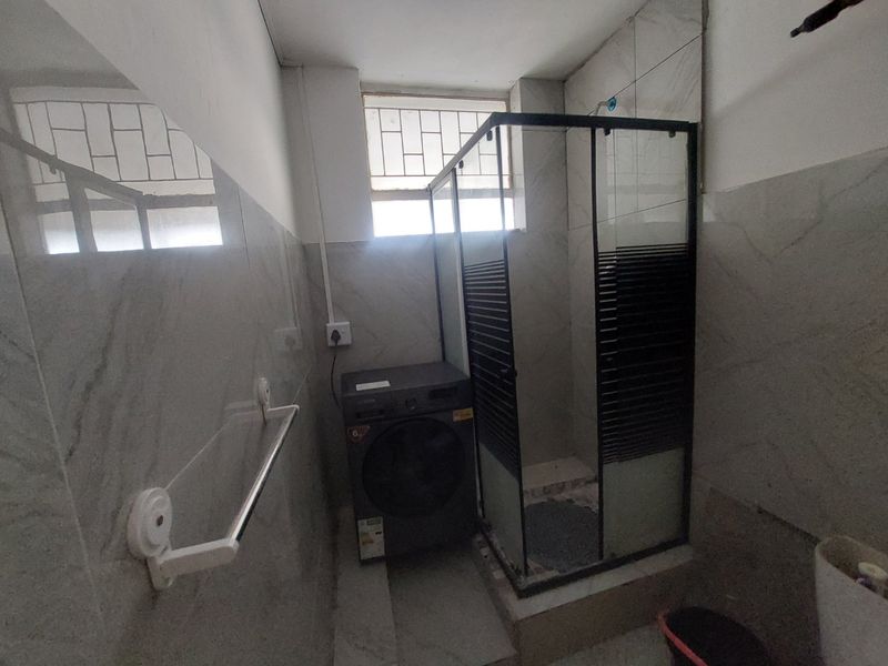 A functional bathroom featuring a glass shower enclosure, tiled wall finishes, and a window with security bars.