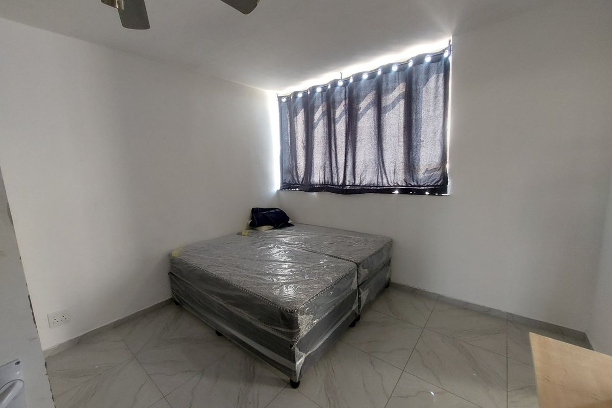 A simple, clean bedroom featuring neutral tiled flooring, a ceiling fan, and natural light from a window with curtains.