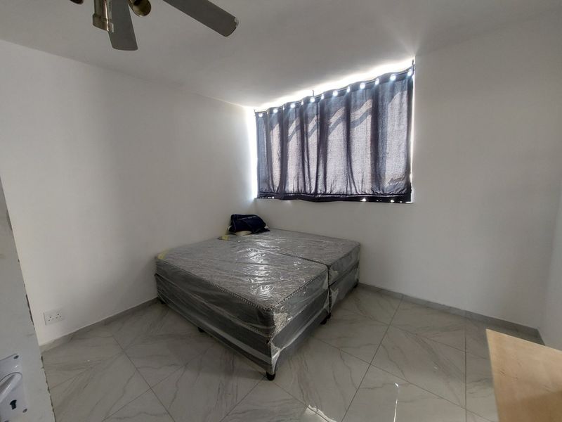 A simple, clean bedroom featuring neutral tiled flooring, a ceiling fan, and natural light from a window with curtains.