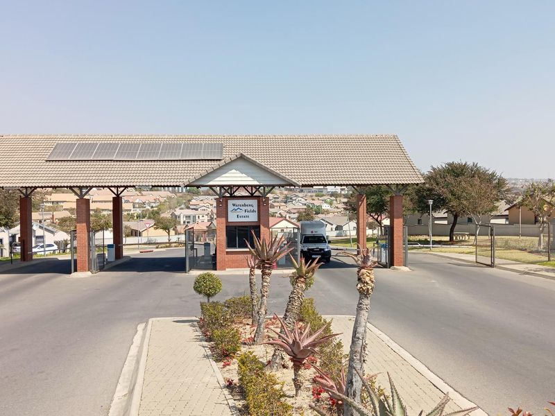 The main entrance gatehouse of Waterberg Fields Estate, featuring a tiled roof with solar panels, brick pillars, and a secure access control point.
