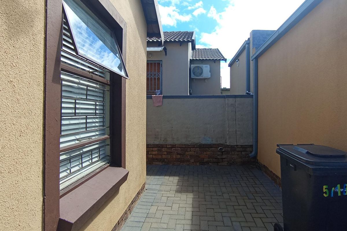 A side courtyard area featuring paved flooring, a brick boundary wall, and security-fitted windows.