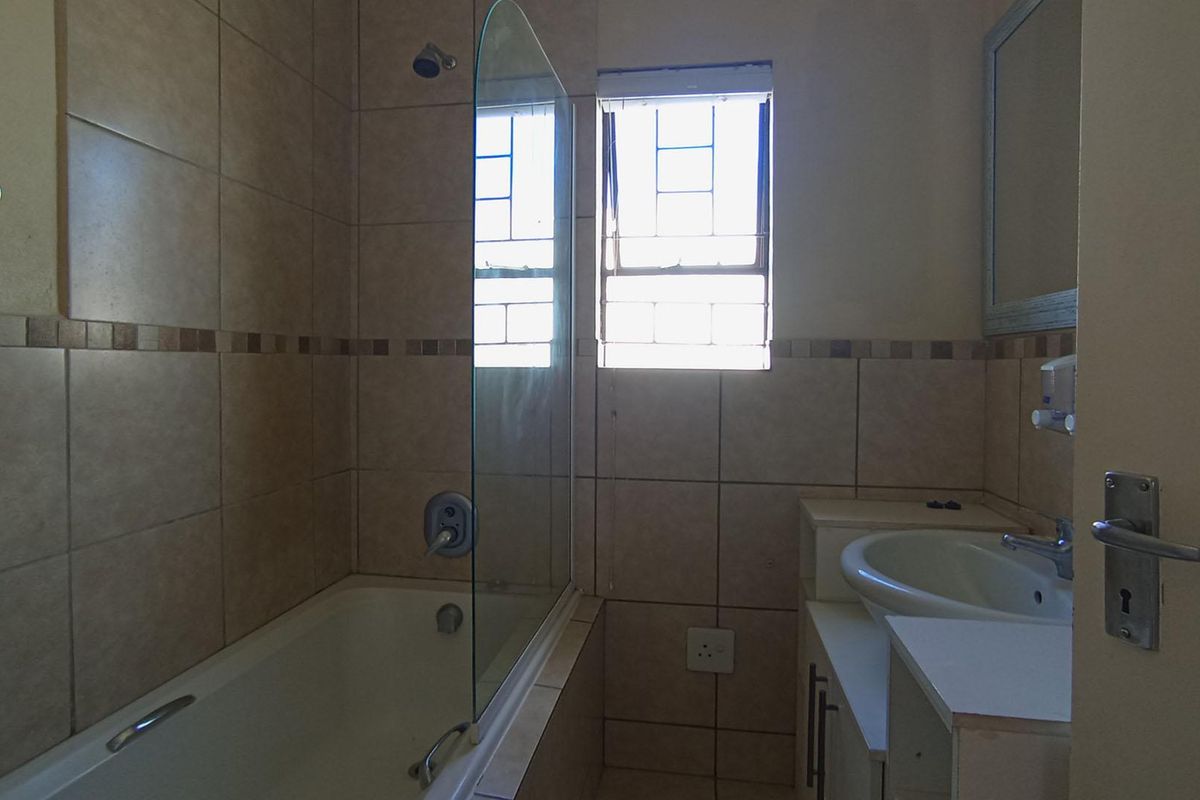 A functional bathroom featuring a bathtub with a glass screen, a vanity unit with a basin, and neutral wall tiling.