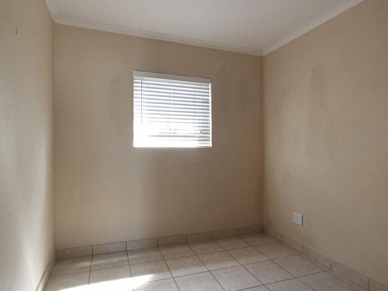 An empty bedroom featuring tiled flooring, neutral walls, and a window fitted with venetian blinds.