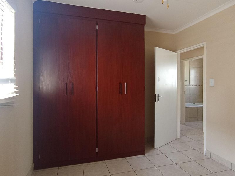 A clean, empty bedroom featuring a large built-in wooden wardrobe, tiled flooring, and direct access to an adjoining bathroom.