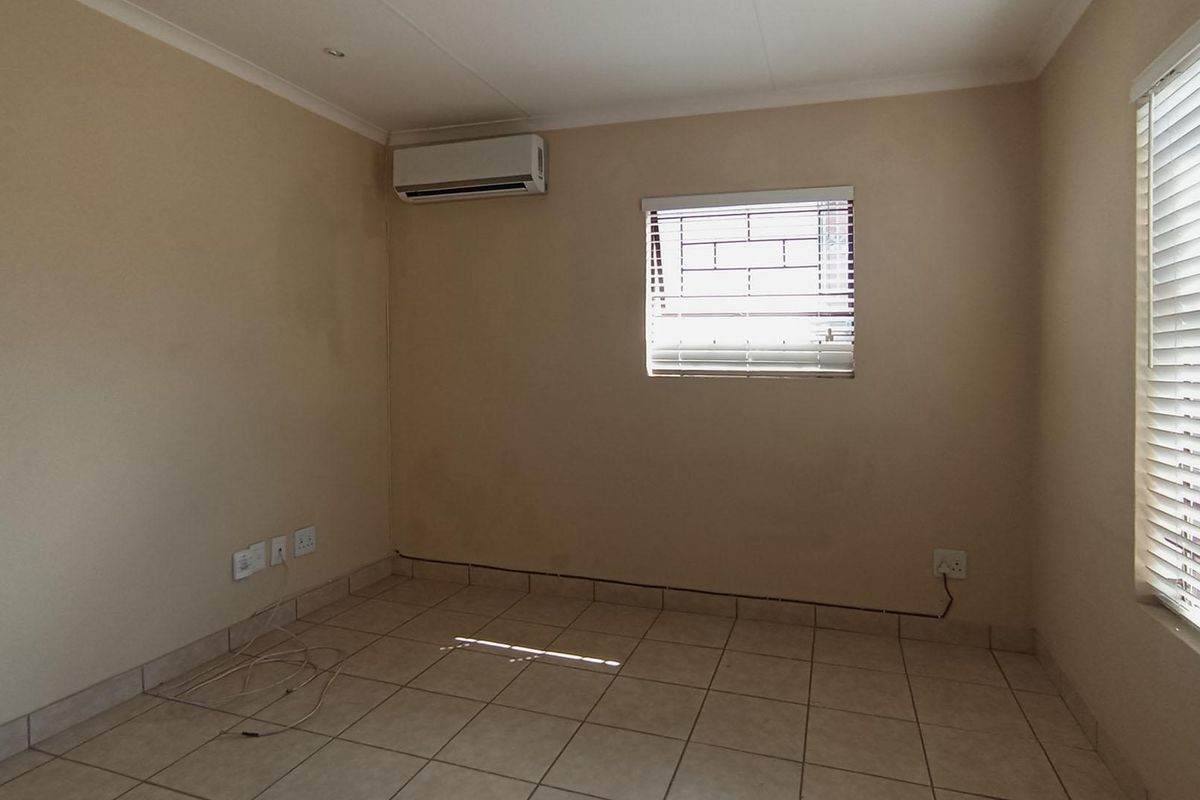 An empty bedroom featuring tiled flooring, a wall-mounted air conditioning unit, and windows fitted with security bars and venetian blinds.