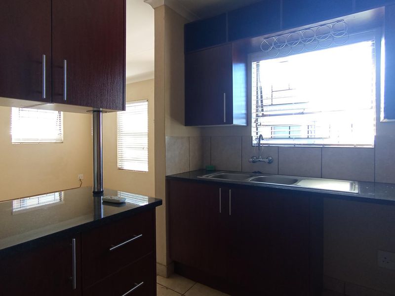 A functional kitchen featuring dark wood cabinetry, granite countertops, a double basin sink, and a tiled backsplash with natural light.
