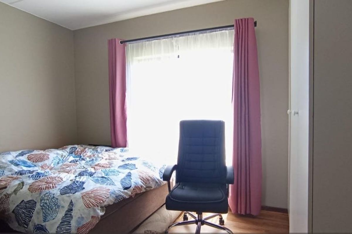A functional bedroom featuring a built-in wardrobe and a large window with curtain rods, providing natural light to the space.