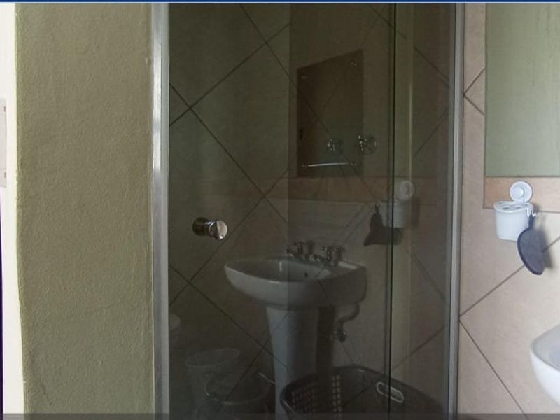A functional bathroom featuring a pedestal basin, a glass-enclosed shower, and tiled wall finishes, offering potential for modernization.