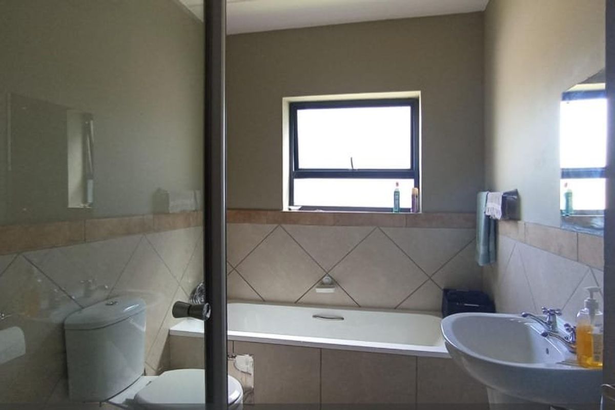 A functional bathroom featuring a built-in bathtub, pedestal washbasin, toilet, and neutral ceramic wall tiling with a window for natural light.