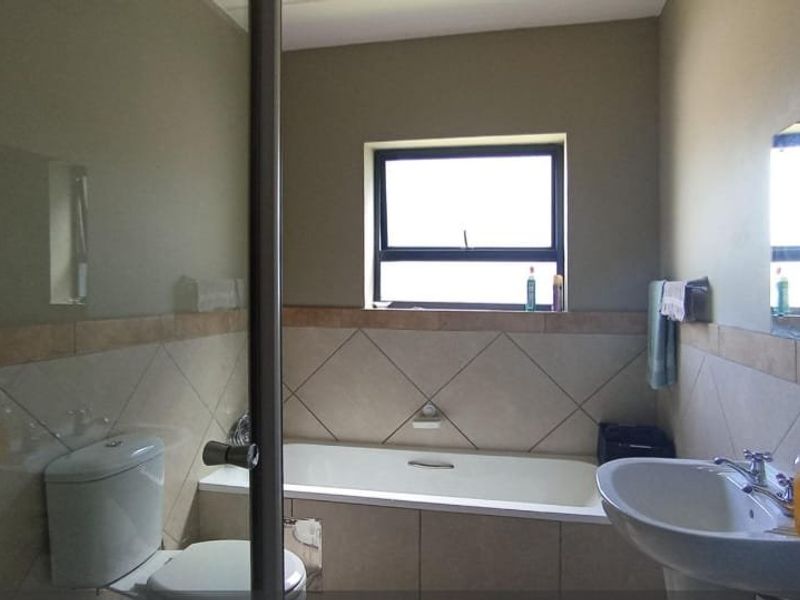 A functional bathroom featuring a built-in bathtub, pedestal washbasin, toilet, and neutral ceramic wall tiling with a window for natural light.